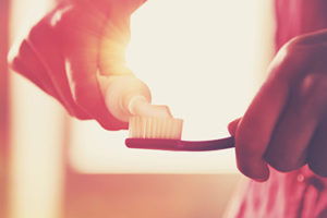 hands holding a toothbrush and placing toothpaste on it in morning sunrise